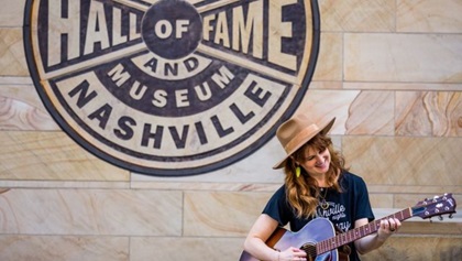 Woman with guitar standing in front of Hall of Fame and Museum in Nashville 