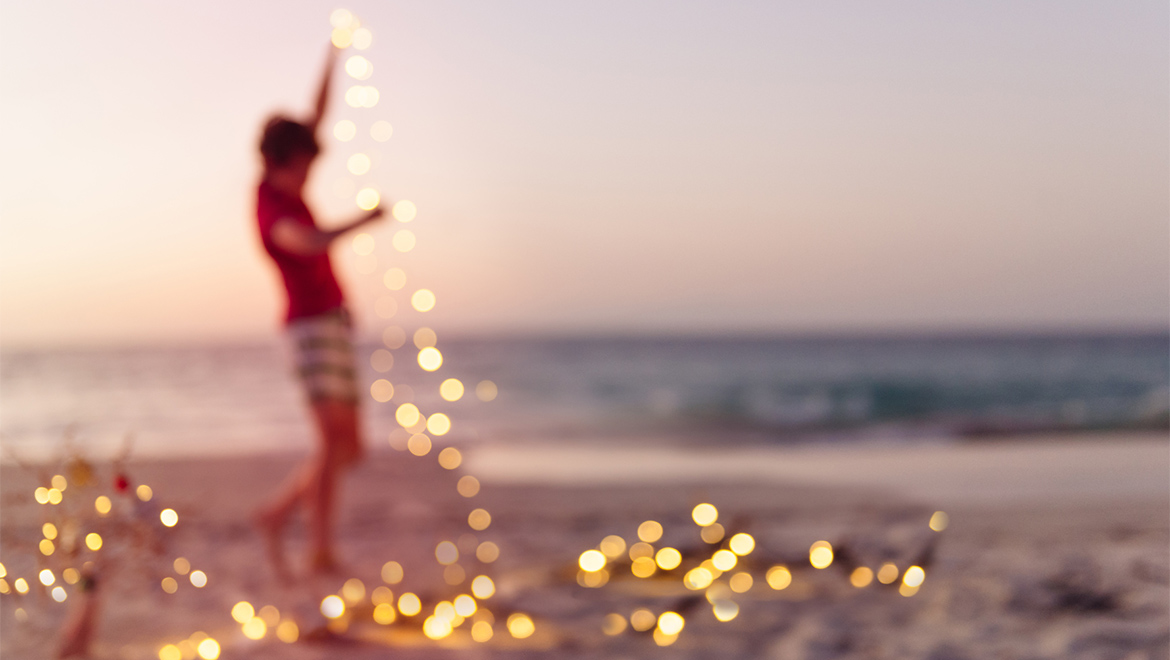 Person on a beach with a string of lights. 