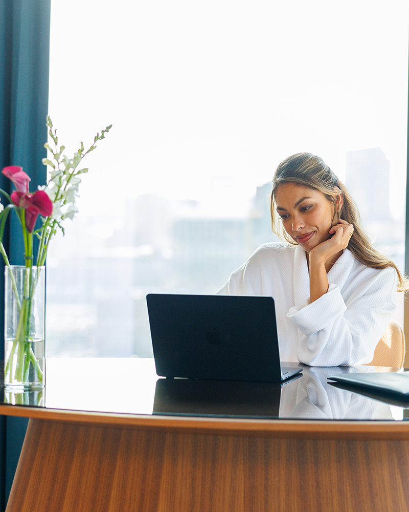 Woman in a bathrobe sitting at desk in a hotel suite