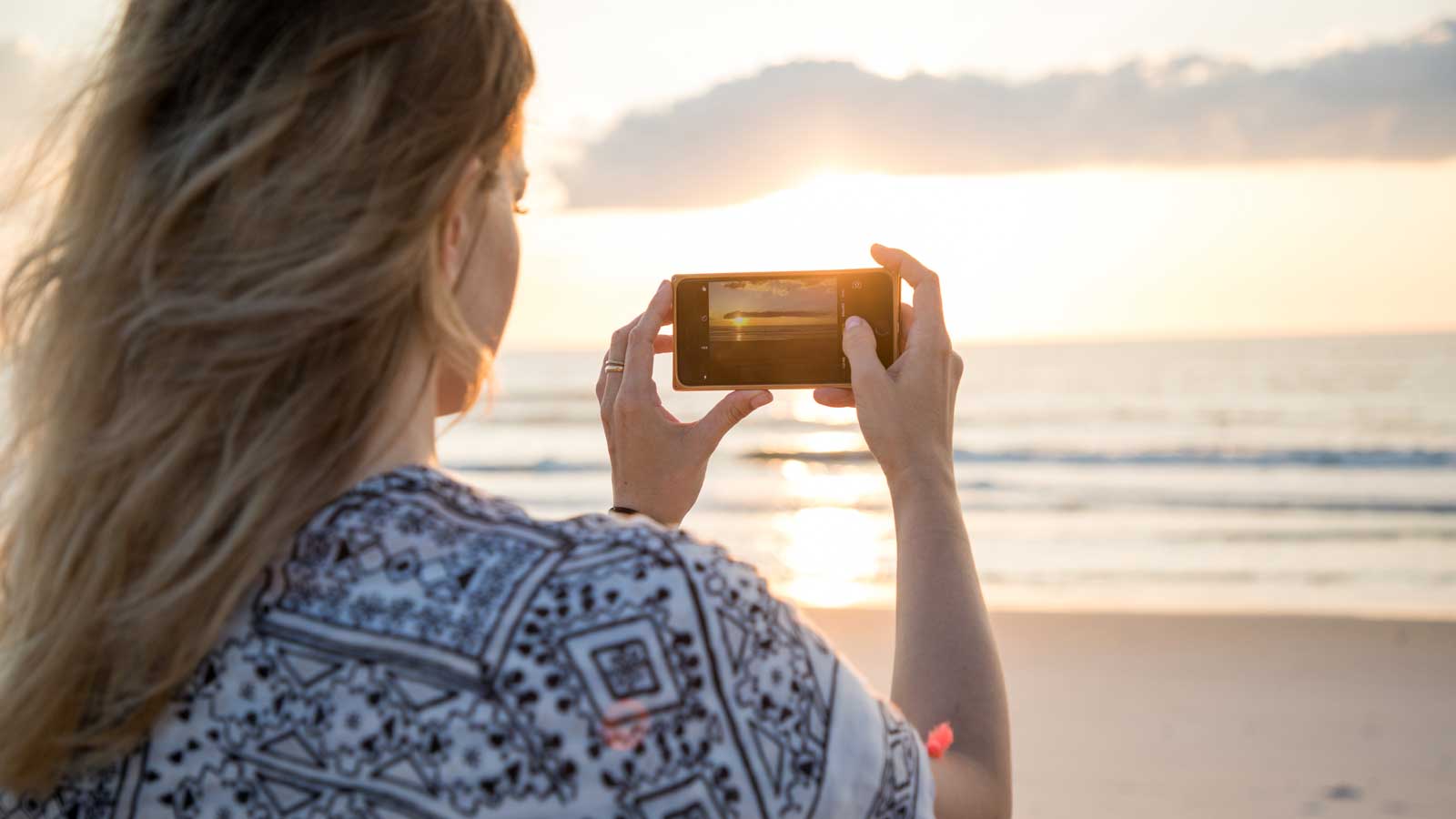 Woman taking a picture of the ocean at sunrise.