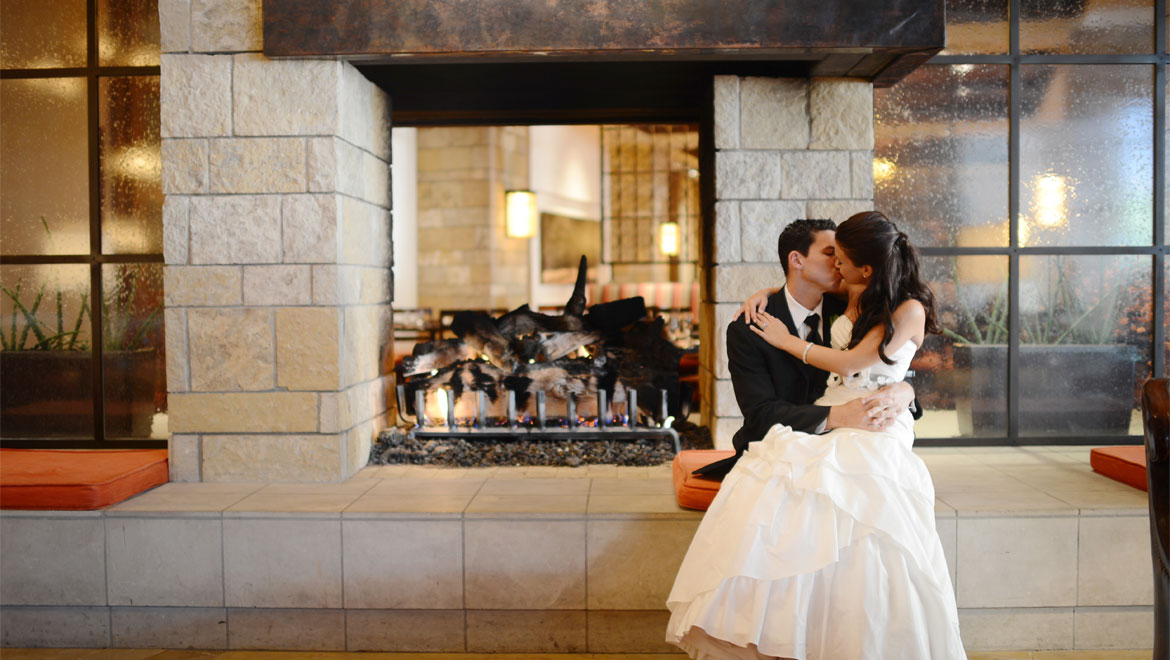 Bride and groom kissing in front of fireplace 