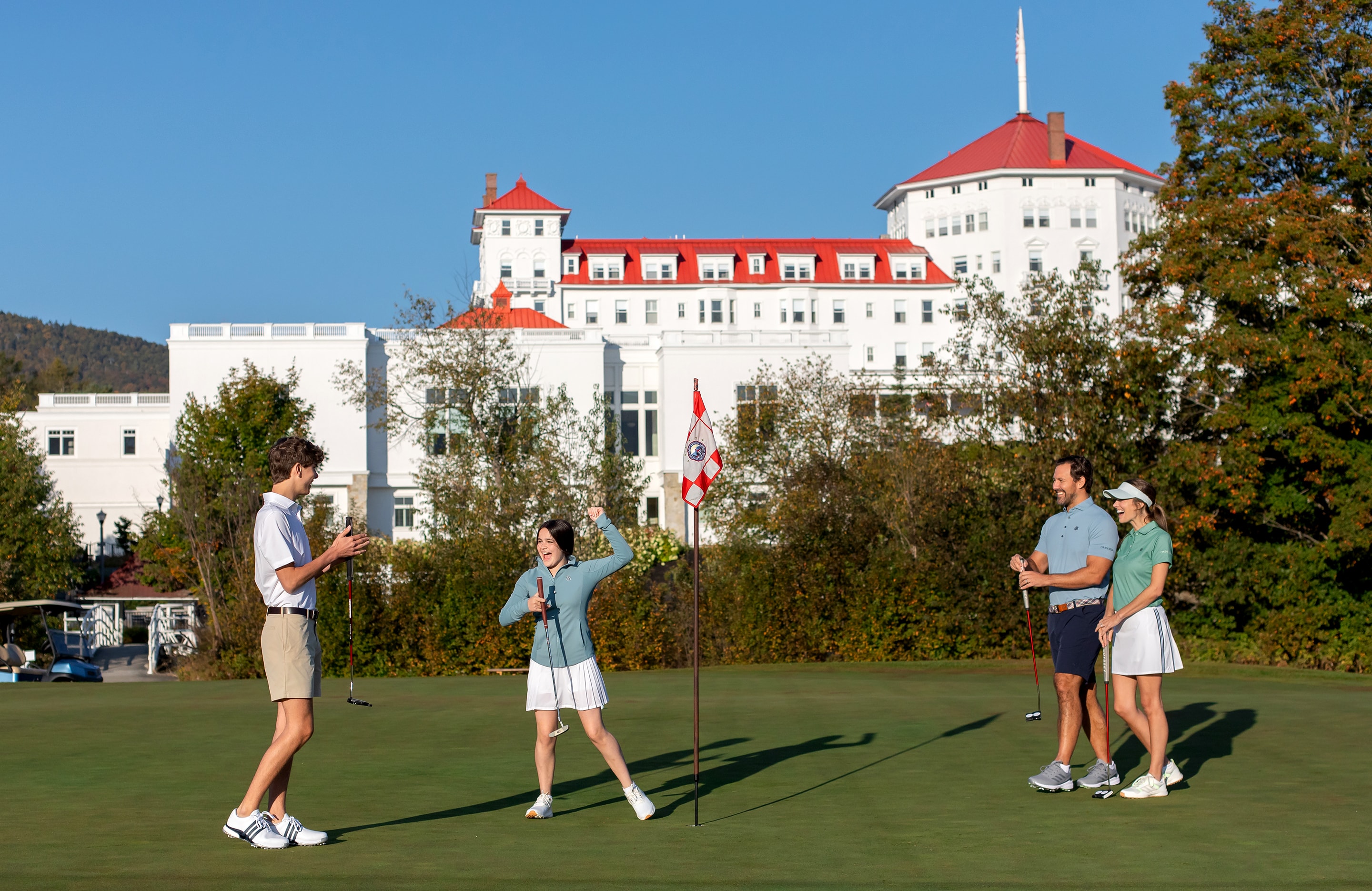 Family of four celebrating on golf course green with a backdrop of the Omni Mount Washington Resort & Spa